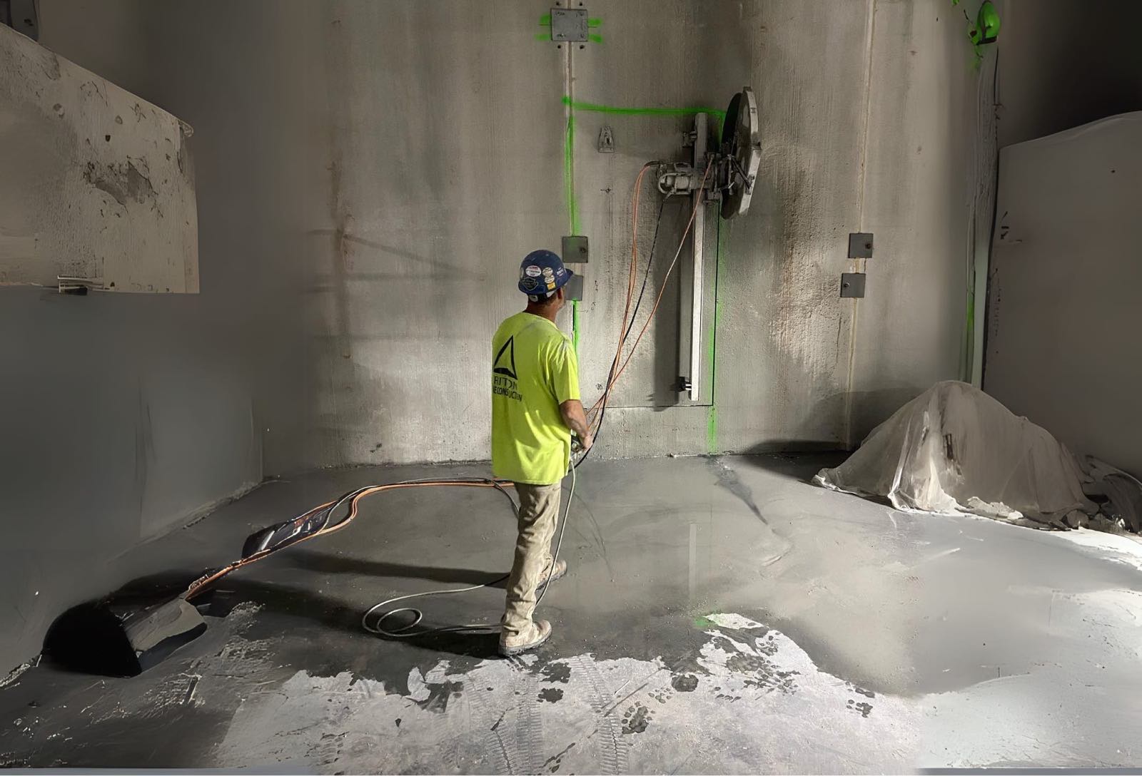 Operator running a track-mounted wall saw through a concrete wall marked out in green layout paint